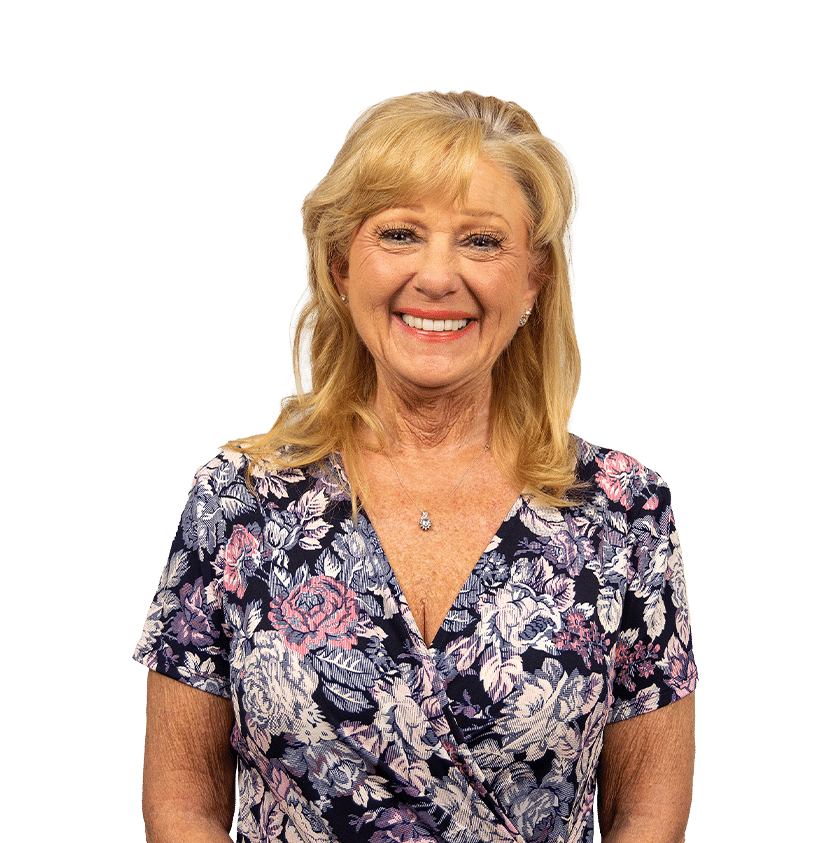 Smiling older woman with blonde hair wearing a navy floral dress, posing for a portrait.