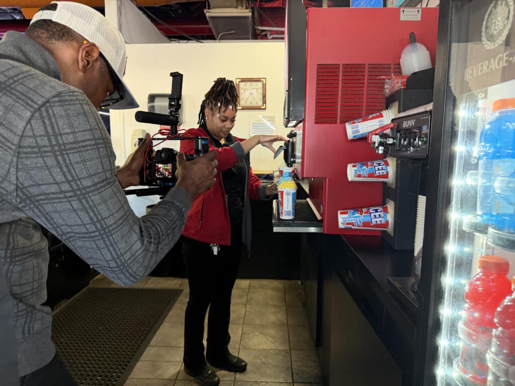 Cameraman records a worker operating a red soda fountain at a fast-food drink counter.
